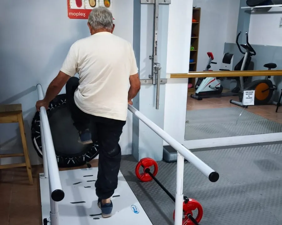 Paciente de espaldas caminando entre barras paralelas sobre la plataforma del estudio de pisada.