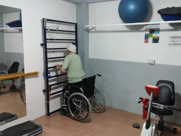 Gimnasio con espaldar, pelotas y bicicleta fija; un paciente hace ejercicio de espaldas.