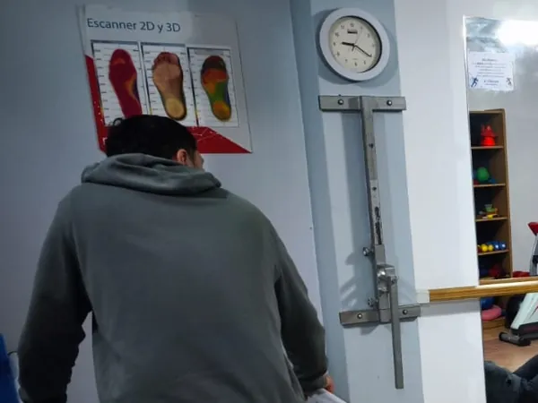 Pasarela del estudio de pisada con el cartel del escáner de pies, y un paciente de espaldas.