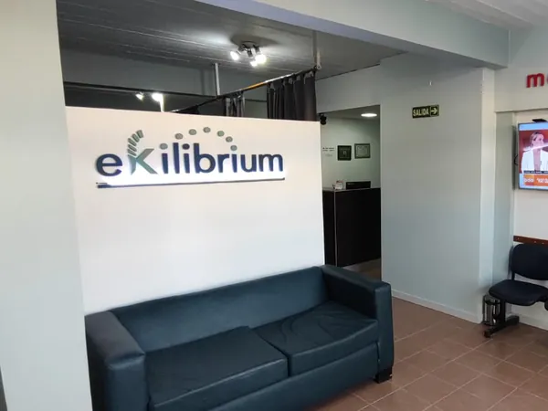 Recepción de Ekilibrium con el logo en la pared, un sillón y sillas de espera.